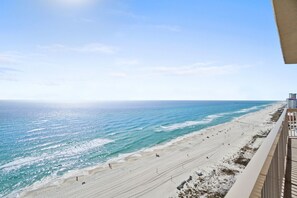 Strandudsigt fra en balkon med klart himmel, sandstrand og en mole i det fjerne.