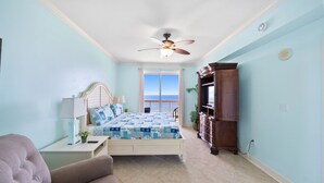 A bedroom with a bed, a nightstand, a dresser, a chair, and a view of the ocean through a sliding door. - Sunrise Beach 1611 Gulf Front Corner Condo Sleeps 10 (Panama City Beach)