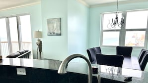 A modern kitchen with a stainless steel sink, black countertops, and a dining area with black chairs. - Sunrise Beach 1611 Gulf Front Corner Condo Sleeps 10 (Panama City Beach)