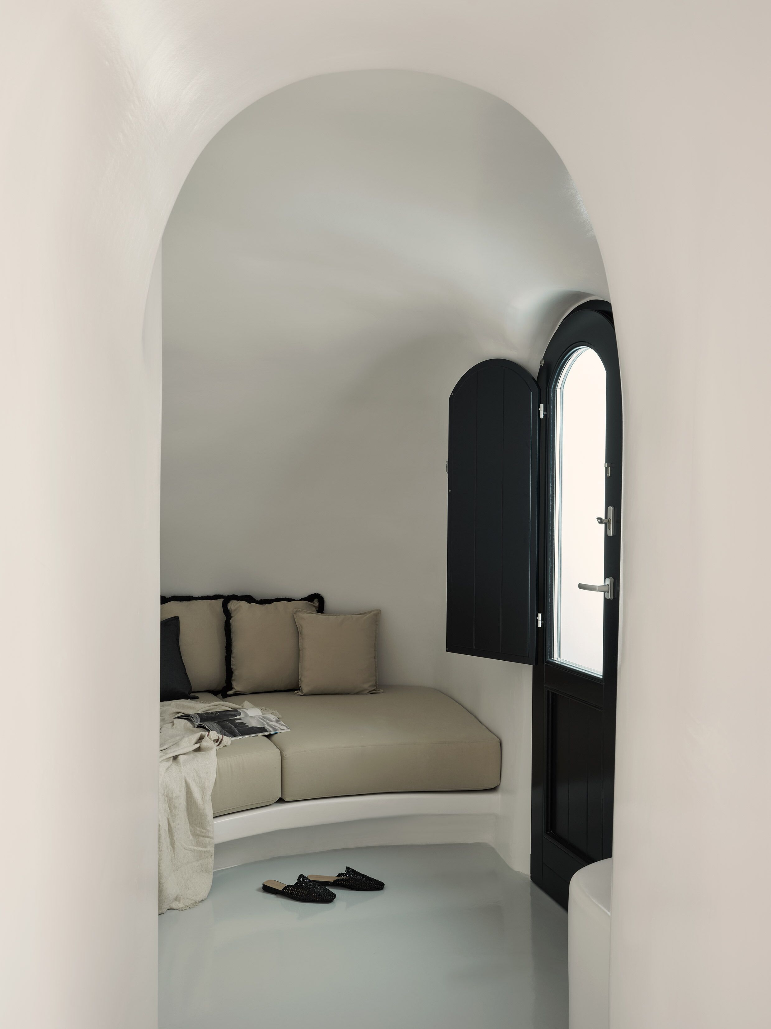 Een kleine kamer met een gebogen plafond, een bed met een beige dekbedovertrek, een zwarte deur en een raam.