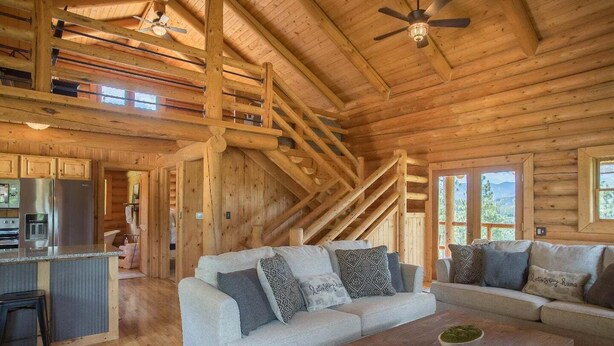 A log cabin interior with a kitchen, a living area with a sofa and coffee table, and a staircase. - Remote Mountain Cabin with Incredible Views (Superior)