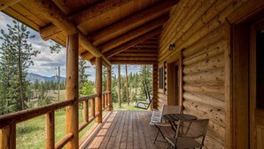 A wooden cabin with a covered porch, a table with chairs, and a view of a forested landscape. - Remote Mountain Cabin with Incredible Views (Superior)