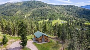 A log cabin with a green roof surrounded by dense forest and hills. - Remote Mountain Cabin with Incredible Views (Superior)