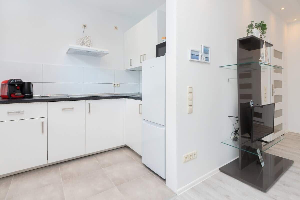 A modern kitchen with white cabinets, a black countertop, and a glass display unit.