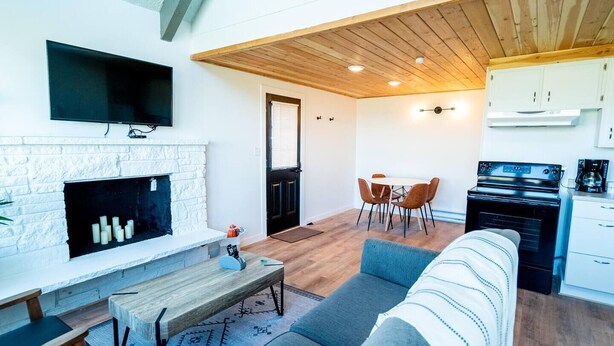 Een moderne woonkamer met een open haard, een eethoek met stoelen, een bank en een keuken met een fornuis.