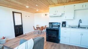 Een compacte keuken met witte kastjes, een zwarte oven en een eethoek met stoelen.