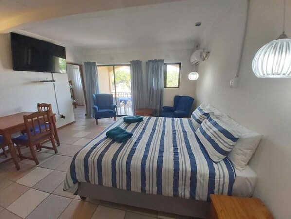 A bedroom with a bed, a desk, chairs, a TV, and a balcony. - Crayfish Inn no.5 (Margate)