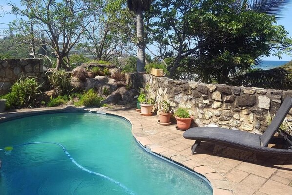 A swimming pool with a stone wall and potted plants, surrounded by lounge chairs.