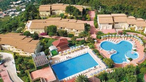 An aerial view of a resort with multiple buildings, a central swimming pool, and a circular pool with a heart-shaped design. - House (Tropea)