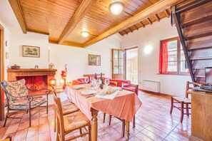 A dining area with a long table set for a meal, wooden chairs, a fireplace, and a staircase.