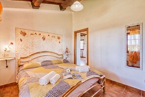 A neatly made bed with a patterned bedspread, a bedside table with a lamp, and a wall with a floral design.