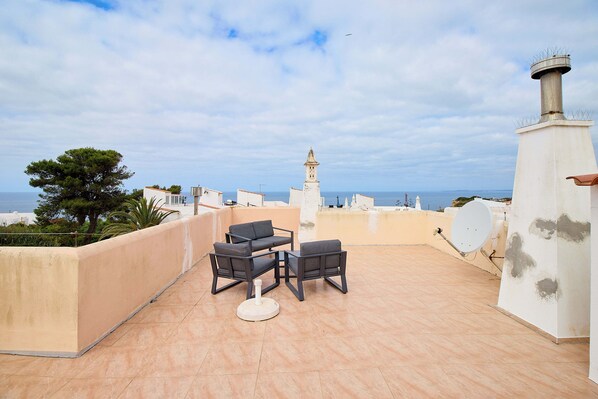 A rooftop terrace with a table and chairs, a satellite dish, and a view of the sea and a tower in the distance. - Apartment Casa Alessandro (Carvoeiro - Vale Centeanes)