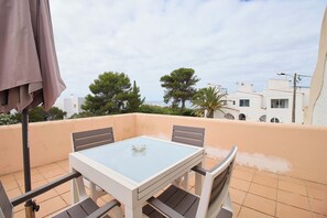 A balcony with a glass table and chairs, a beige wall, and a view of trees and buildings. - Apartment Casa Alessandro (Carvoeiro - Vale Centeanes)