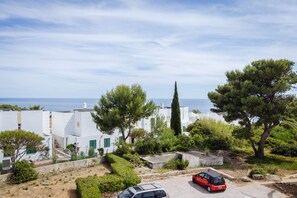 A coastal residential area with white buildings, a red car parked on the street, and a view of the sea in the background. - Apartment Casa Alessandro (Carvoeiro - Vale Centeanes)