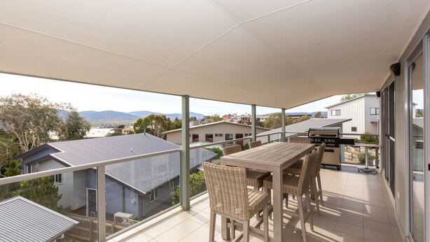 A balcony with a table and chairs, a grill, and a view of houses and mountains. - Reedy's Run - 11 Reedy's Cutting (Jindabyne)