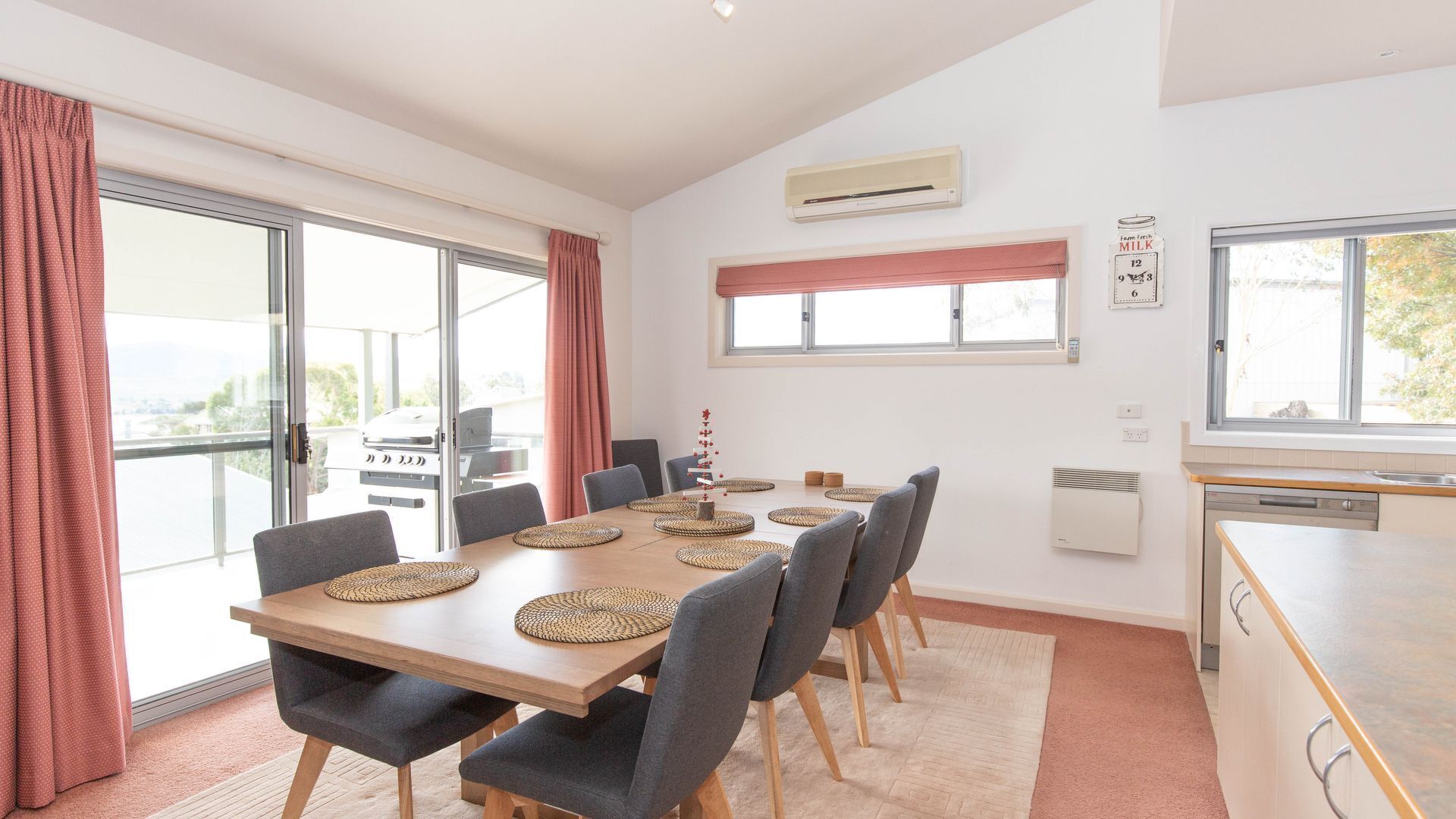 A dining area with a wooden table, grey upholstered chairs, and woven placemats.