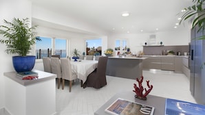 A modern kitchen with white cabinets, a large island, and a dining area with a table and chairs. - AMORE RENTALS - Villa Ligea with Private Swimming Pool, Sea View and Parking (Sant´Agata sui Due Golfi)