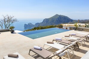 Un espace aménagé au bord de la piscine, avec des chaises longues et une vue sur la mer et les montagnes.