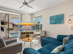 A living room with a TV, sofa, armchair, and a painting on the wall.
