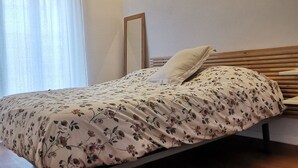Een slaapkamer met een bed, houten balken, een hanglamp en een raam met gordijnen.