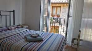 Een slaapkamer met een bed, een nachtkastje en een raam met uitzicht op een balkon.