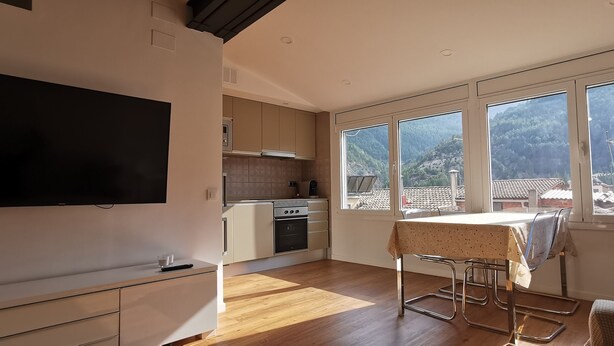 Een moderne keuken met een groot raam, houten vloeren en een eethoek met een tafel en stoelen.