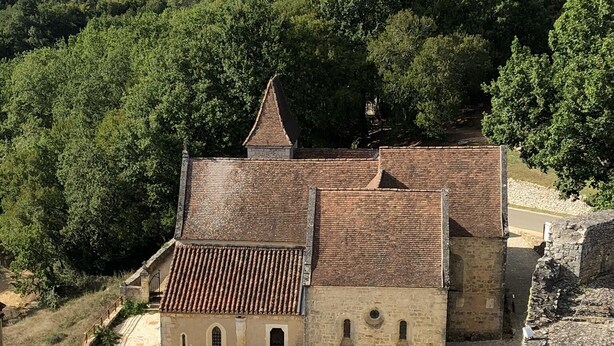 A historic building with a tiled roof and stone walls, surrounded by a stone fortification and lush greenery.