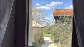 A window with a view of a courtyard, a stone building, and a clear blue sky.