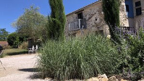 A rustic stone building with a balcony, surrounded by tall grasses and lavender plants.