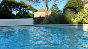 A swimming pool with clear water, surrounded by greenery and a building in the background.