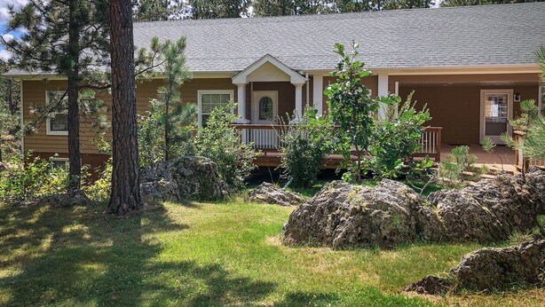 Una casa de dues plantes amb un porxo, envoltada d'arbres i roques.