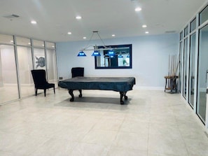 Une pièce moderne équipée d’une table de billard, d’un fauteuil et d’une lampe fixée au mur.