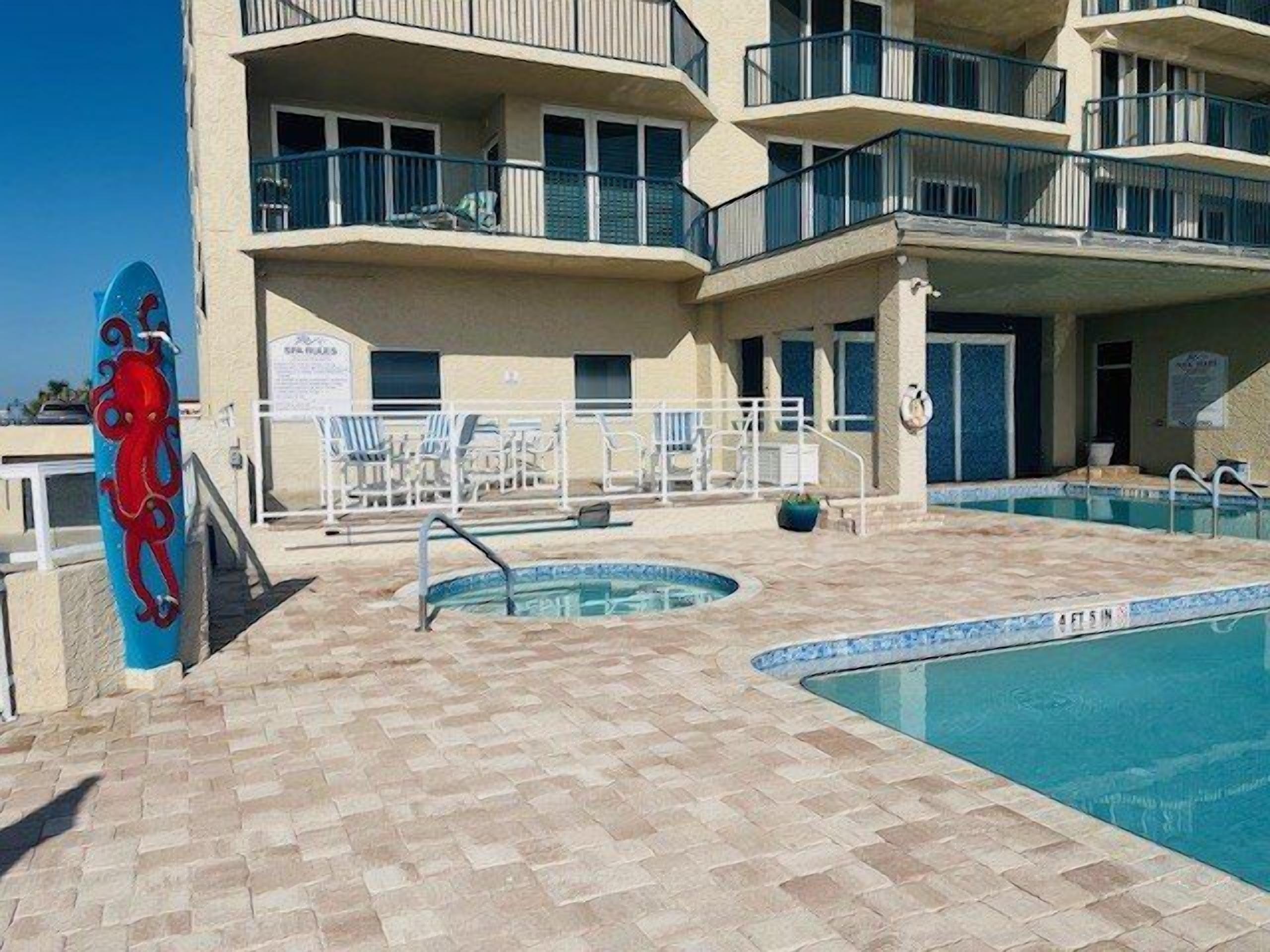 A pool area with a blue octopus decoration, lounge chairs, and a building with multiple balconies.