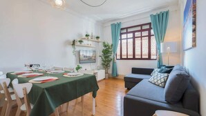 A dining area with tables set for four, a sofa, and a window with curtains.