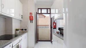 A narrow kitchen with white cabinets, a stove, and a microwave. There is a fire extinguisher on the wall and a small plant on the counter.