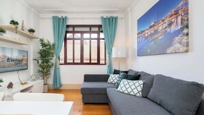 A modern living room with a grey sofa, teal curtains, a painting of a bridge, and a TV on the wall.