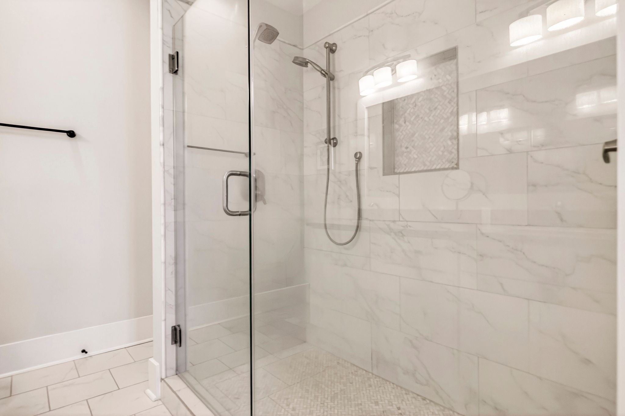 Une salle de bain moderne avec une douche à parois de verre, des carreaux de marbre et un porte-serviettes.