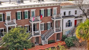 A multi-story brick building with a central staircase, a red door, and a balcony with railings. - Perfect Modern Getaway with Parking Steps to Forsyth by Lucky Savannah (Savannah)