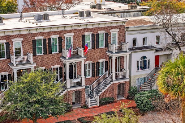 A multi-story brick building with a central staircase, a red door, and a balcony with railings. - Perfect Modern Getaway with Parking Steps to Forsyth by Lucky Savannah (Savannah)