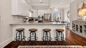 A modern kitchen with white cabinets, a central island with stools, stainless steel appliances, and a chandelier. - Perfect Modern Getaway with Parking Steps to Forsyth by Lucky Savannah (Savannah)
