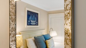 Ein Schlafzimmer mit Bett, Kissen, Nachttisch, Lampe und einem gerahmten Bild an der Wand.