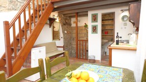 Une cuisine chaleureuse avec un escalier en bois, une table à manger sur laquelle se trouve un panier de fruits et un mur en pierre.