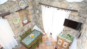 Une pièce aux murs de pierre, avec une table et des chaises, un téléviseur et un petit meuble contenant des objets décoratifs.
