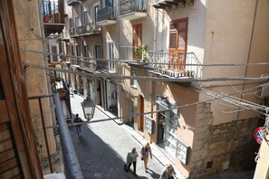 Une rue étroite, bordée de bâtiments des deux côtés, avec des balcons dotés de balustrades et une enseigne indiquant l’emplacement d’un magasin.