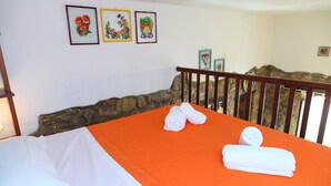 Une chambre d’hôtel avec un lit, une couverture orange, deux serviettes enroulées et trois œuvres d’art florales encadrées accrochées au mur.