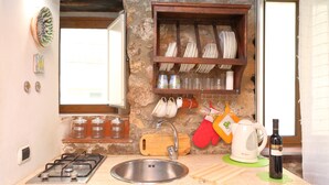 Une cuisine avec un mur en pierre, une étagère en bois où sont rangés de la vaisselle, une cuisinière à gaz et un évier.
