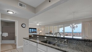 A modern kitchen with granite countertops, stainless steel appliances, and a large window offering a view of the ocean. - Steps from the beach! Pool, Pickleball, and Tennis Courts! (Miramar Beach)