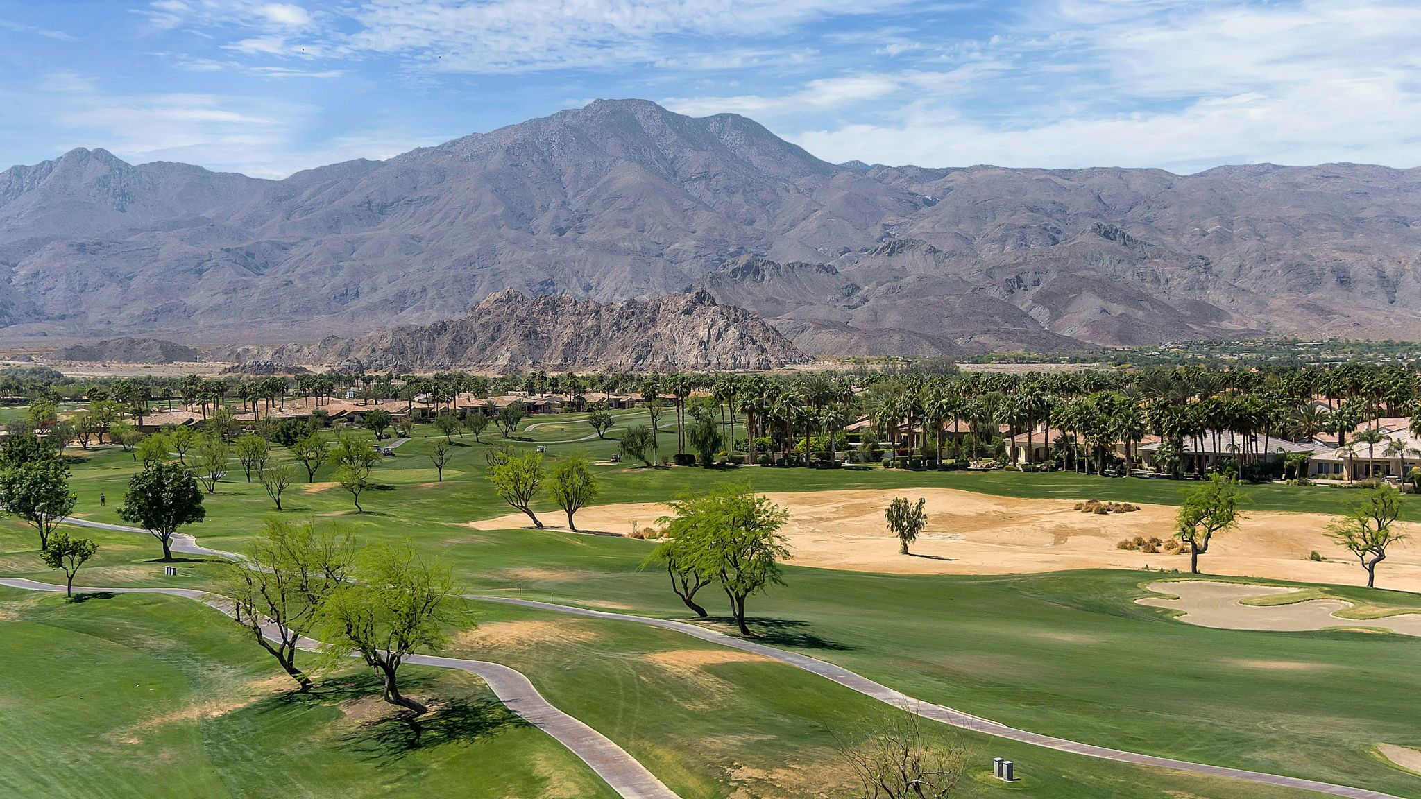 A golf course with a mountain backdrop, well-maintained fairways, and a clear sky.