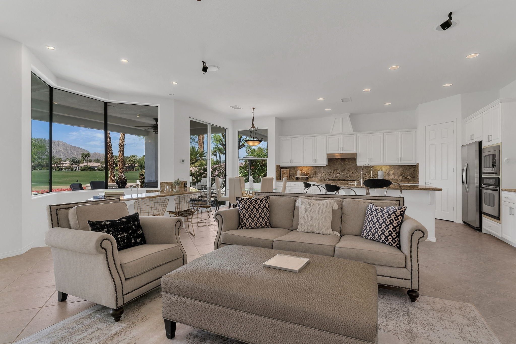 A spacious living area with a large window, a kitchen with white cabinets, and a dining area with a table and chairs.