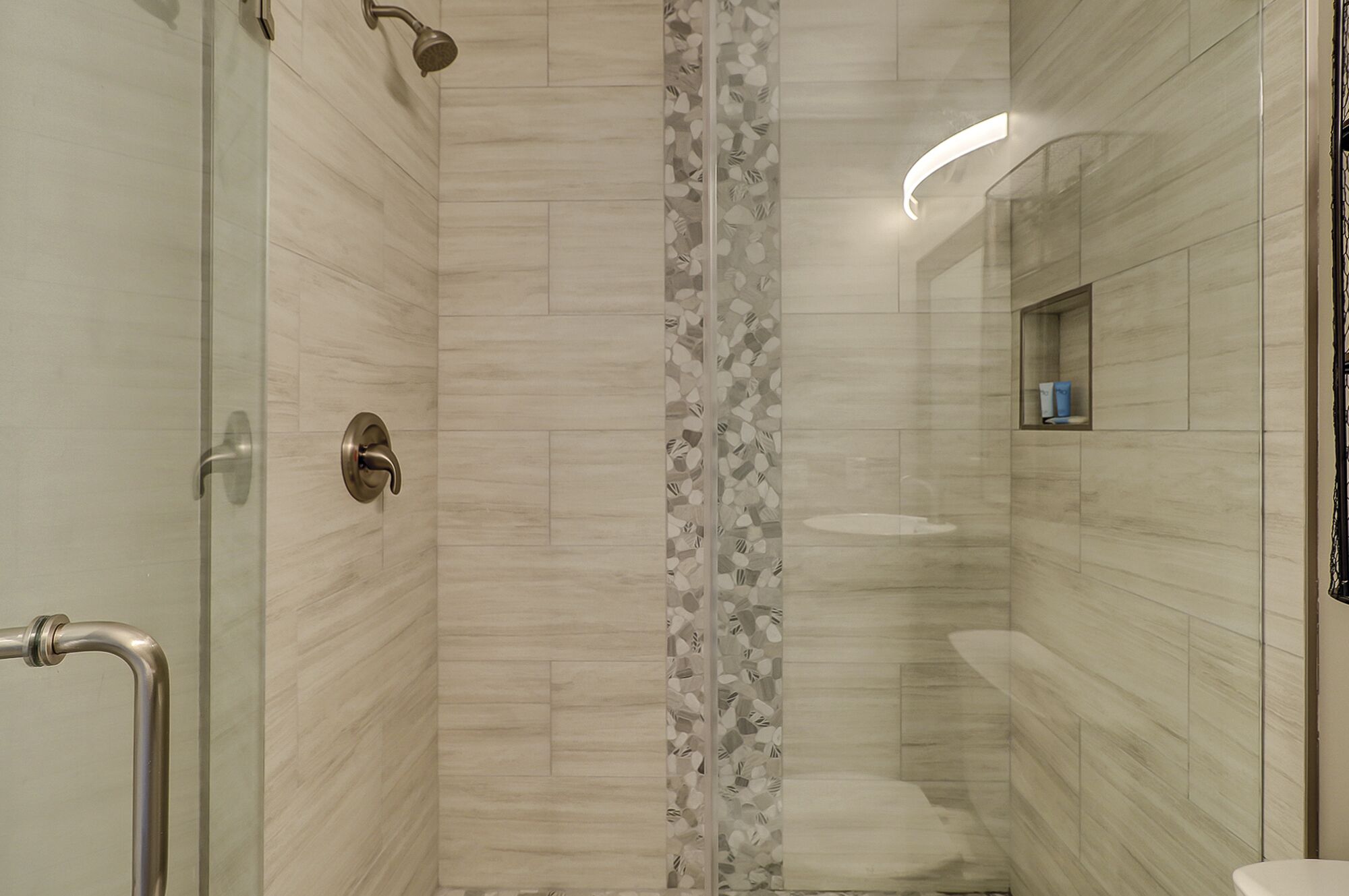 A modern bathroom with a shower, a glass door, a toilet, and a small shelf with toiletries.